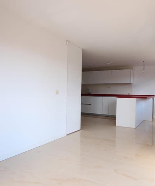 Interior vacío de un apartamento moderno, paredes blancas, suelo claro, vista parcial de la cocina con encimera roja.