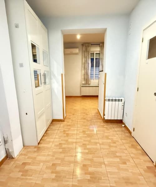 Pasillo con suelo de baldosas que conduce a una habitación con ventana, armario blanco a la izquierda y puerta blanca a la derecha.