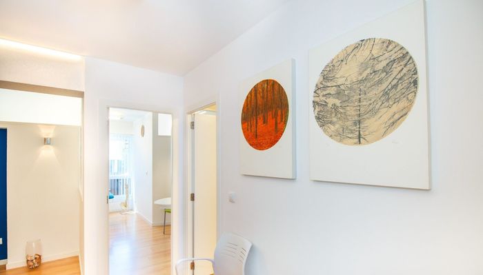 Habitación luminosa de color azul y blanco con dos camas individuales, estanterías y una pequeña zona de comedor al fondo.