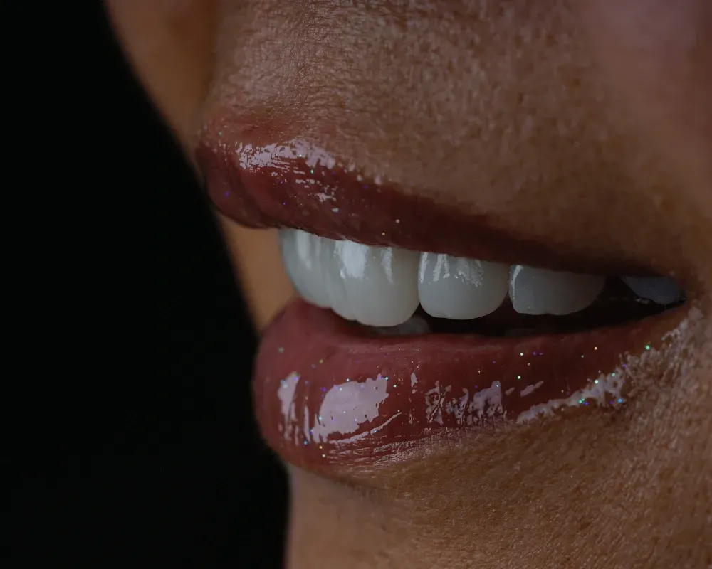 Primer plano de unos labios brillantes de color rojo oscuro con dientes blancos visibles sobre un fondo negro.