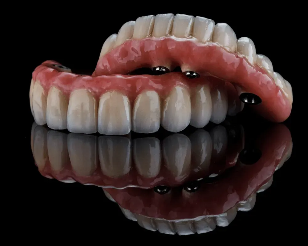 Primer plano de una dentadura postiza con encías rojas, reflejadas en una superficie negra brillante.