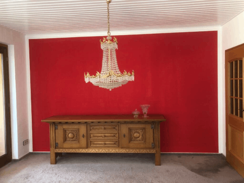 Ein leerer Raum mit einer roten Wand und einem Kronleuchter, der von der Decke hängt.