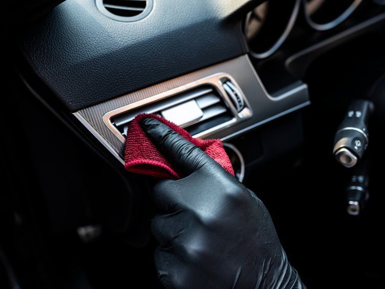 Una persona que lleva guantes negros está limpiando la rejilla de ventilación de un coche.