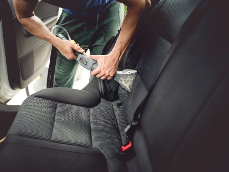 Un hombre está limpiando el asiento trasero de un coche con una aspiradora.