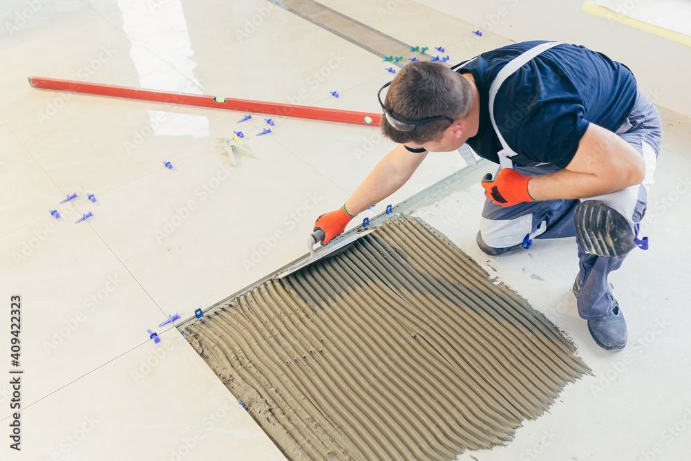 Un homme pose des carreaux de sol, étalant le mortier avec une truelle crantée.