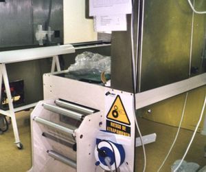 Una máquina de retractilado en una fábrica. Contiene señales de advertencia.