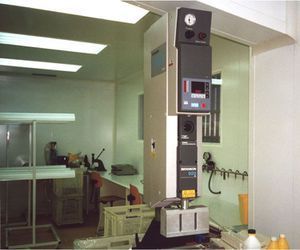 Máquina industrial en una sala blanca. Cuenta con panel de control, indicadores y base rectangular.