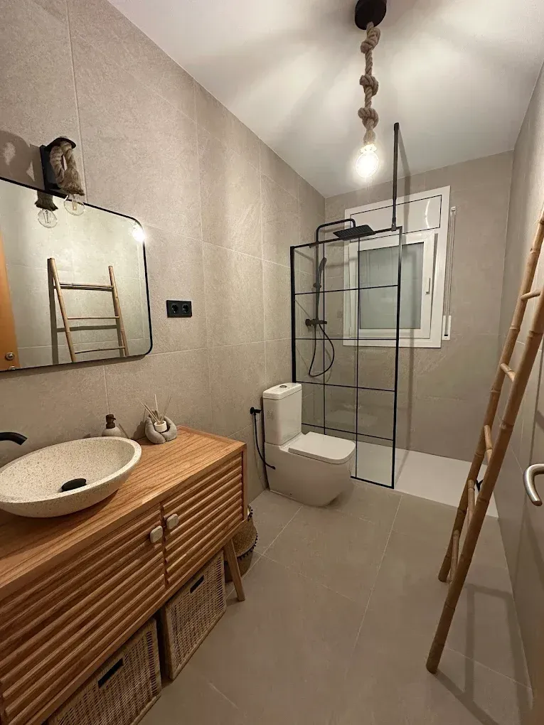 Baño con tocador de madera, lavabo, ducha, inodoro y escalera de bambú.