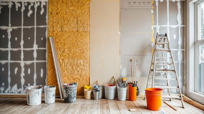 Rénovation intérieure avec outils, pots de peinture et échelle contre un mur partiellement construit près de la fenêtre.