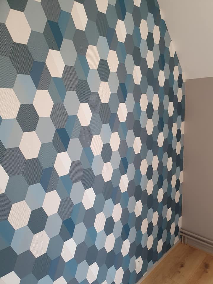 Papier peint hexagonal bleu, gris et blanc sur un mur incurvé au-dessus d'un parquet.