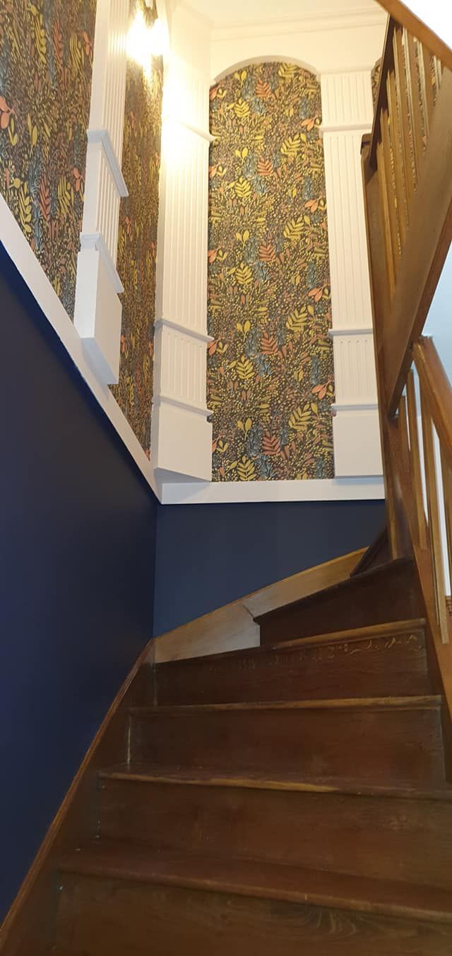 Escalier en bois courbé, murs bleu marine et papier peint fleuri dans un couloir intérieur étroit