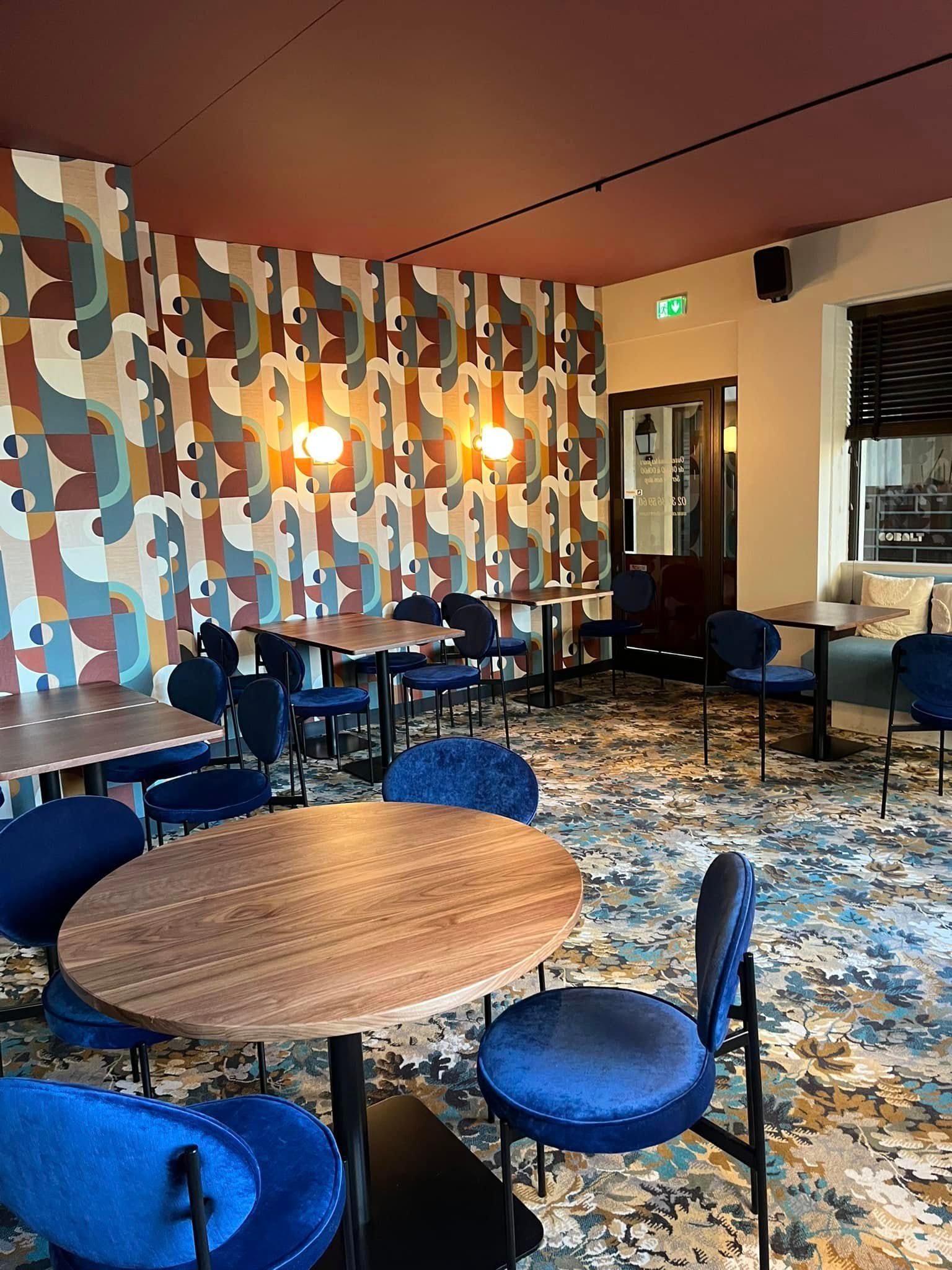 Salon de café vide avec chaises bleues, tables rondes, papier peint à motifs et éclairage chaleureux