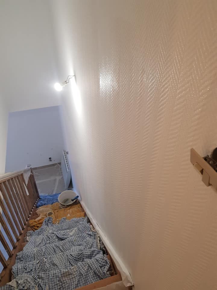Escalier étroit avec rampe en bois, moquette bleue et sol recouvert de plastique menant à un palier en contrebas