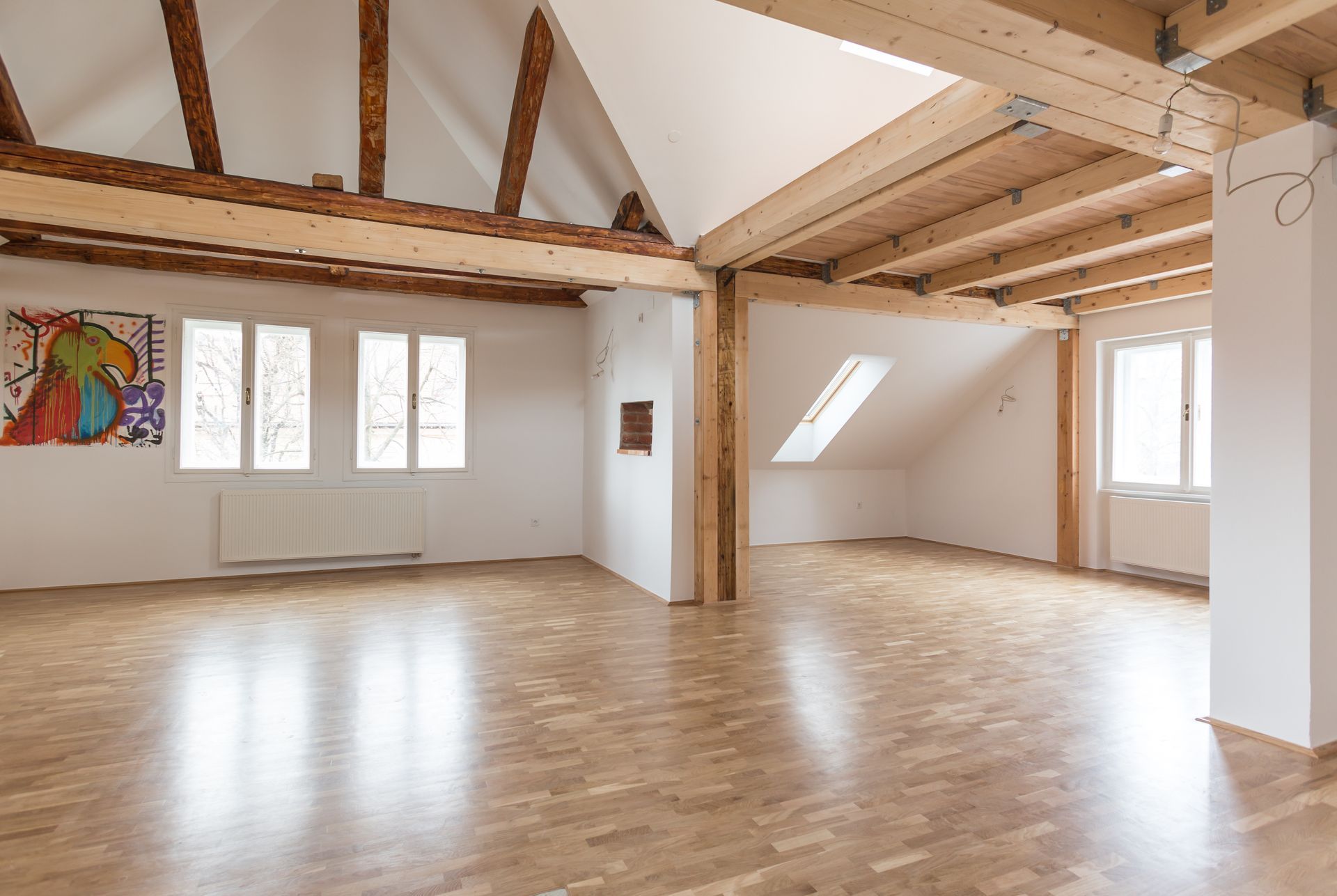 Loft spacieux et vide avec poutres apparentes, puits de lumière et parquet ciré, baigné de lumière naturelle.