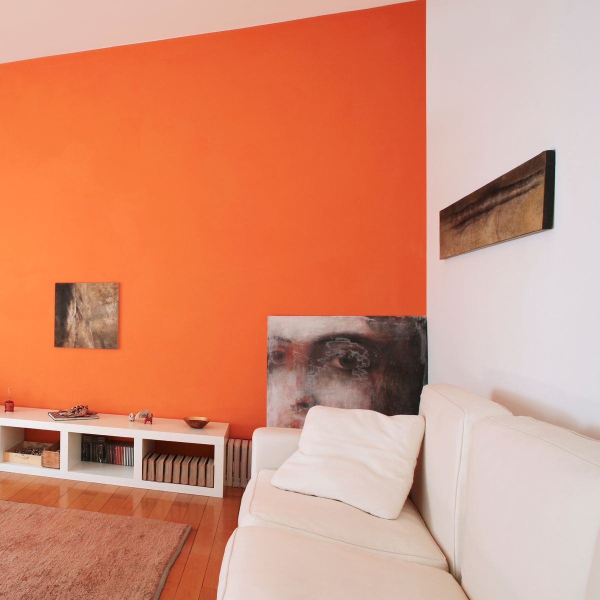 Salon moderne avec un mur d'accent orange, un canapé blanc, des étagères basses et une œuvre d'art murale abstraite.