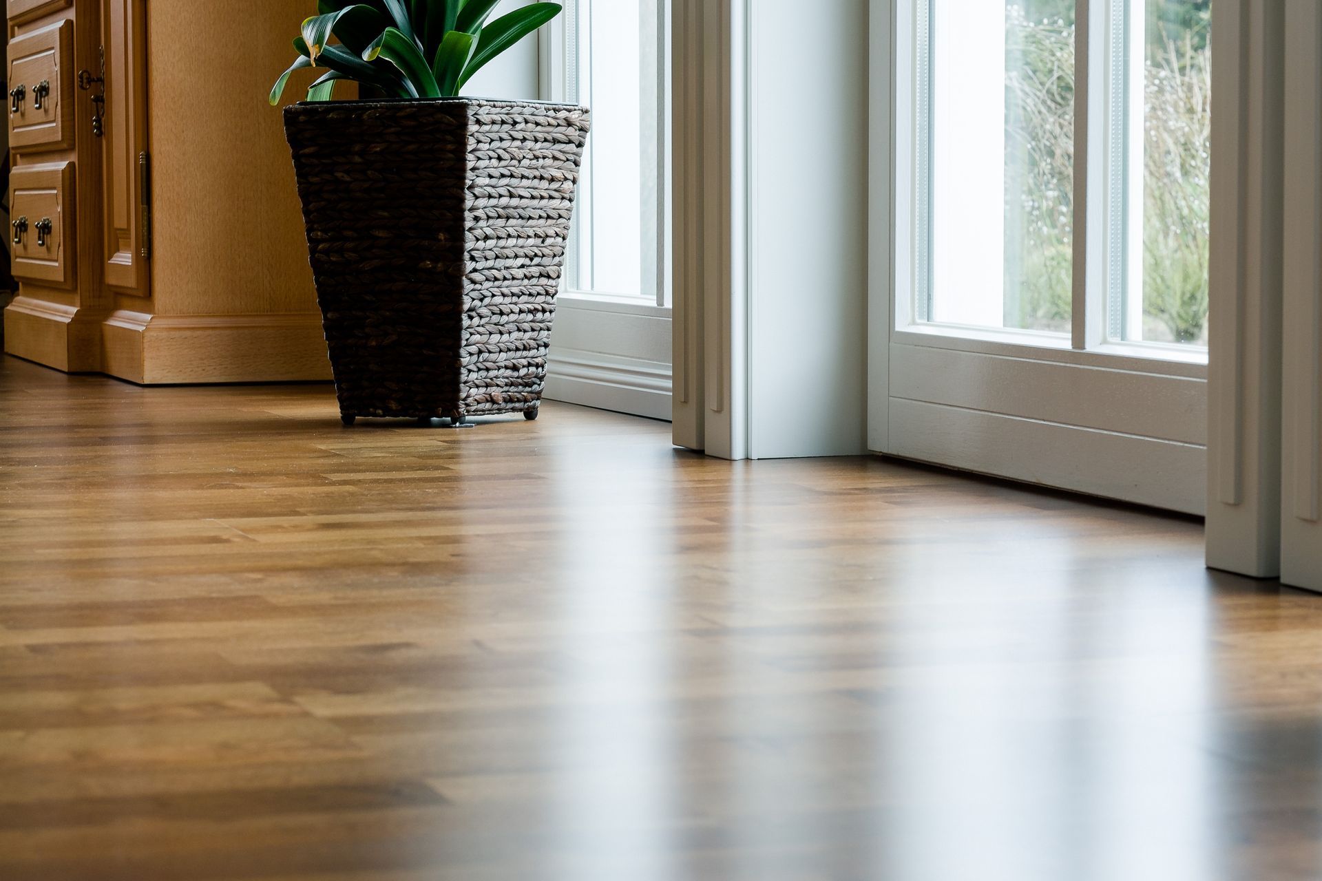 Parquet baigné de soleil près d'une porte-fenêtre coulissante, avec un pot en osier et une plante d'intérieur près d'un meuble