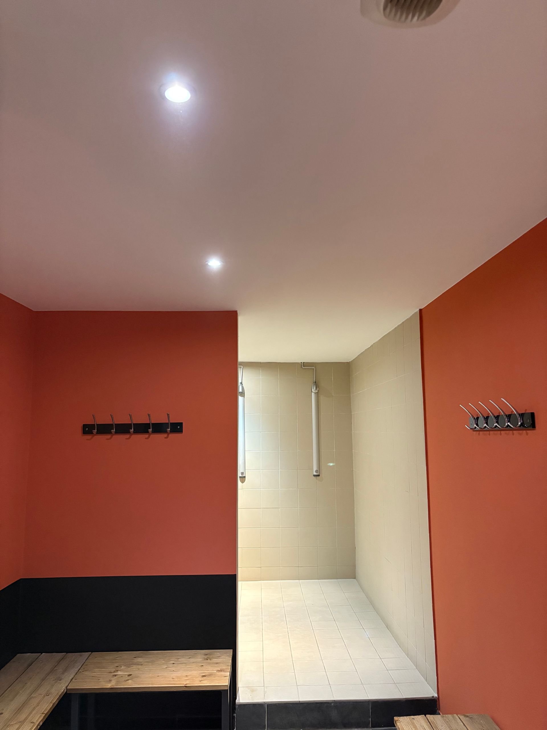 Petite pièce aux murs orange et beige, banc noir, table en bois et un couloir lumineux derrière une porte blanche.
