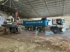 Un camión volquete está estacionado en un almacén al lado de una excavadora.