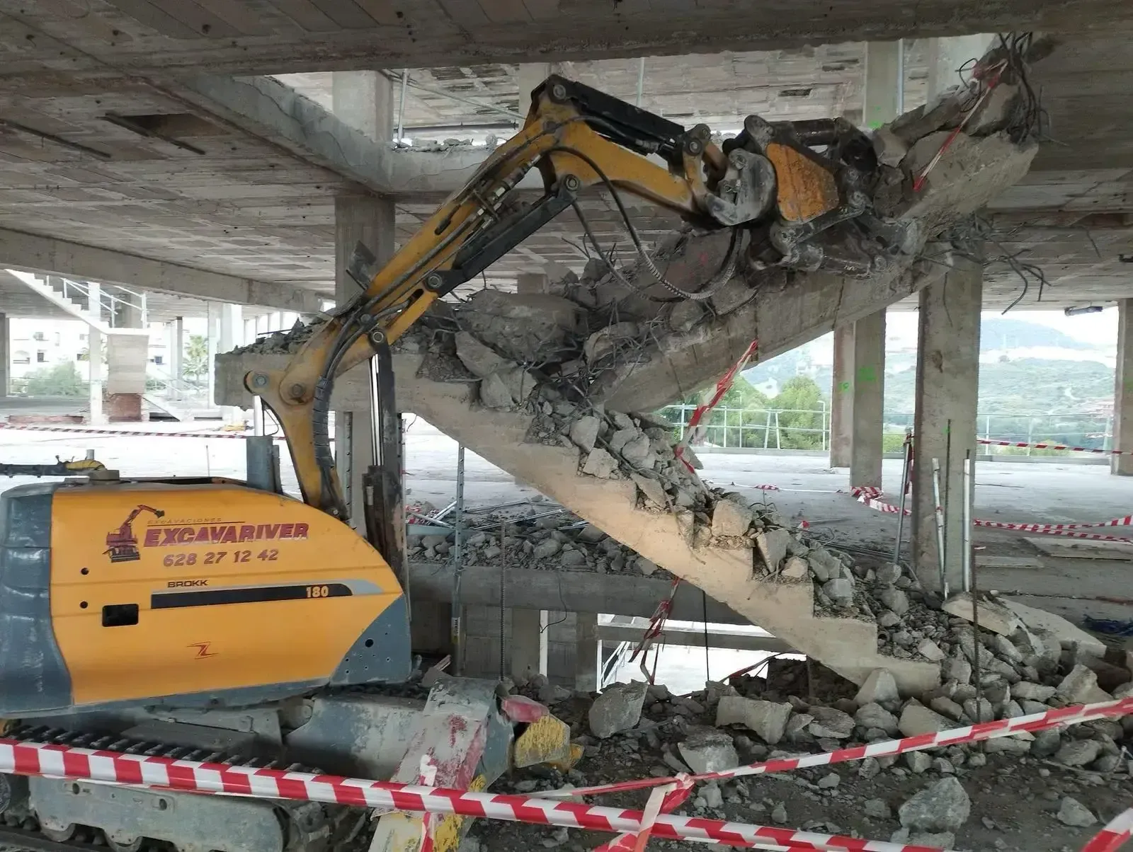 Una excavadora amarilla está demoliendo un conjunto de escaleras en un edificio.