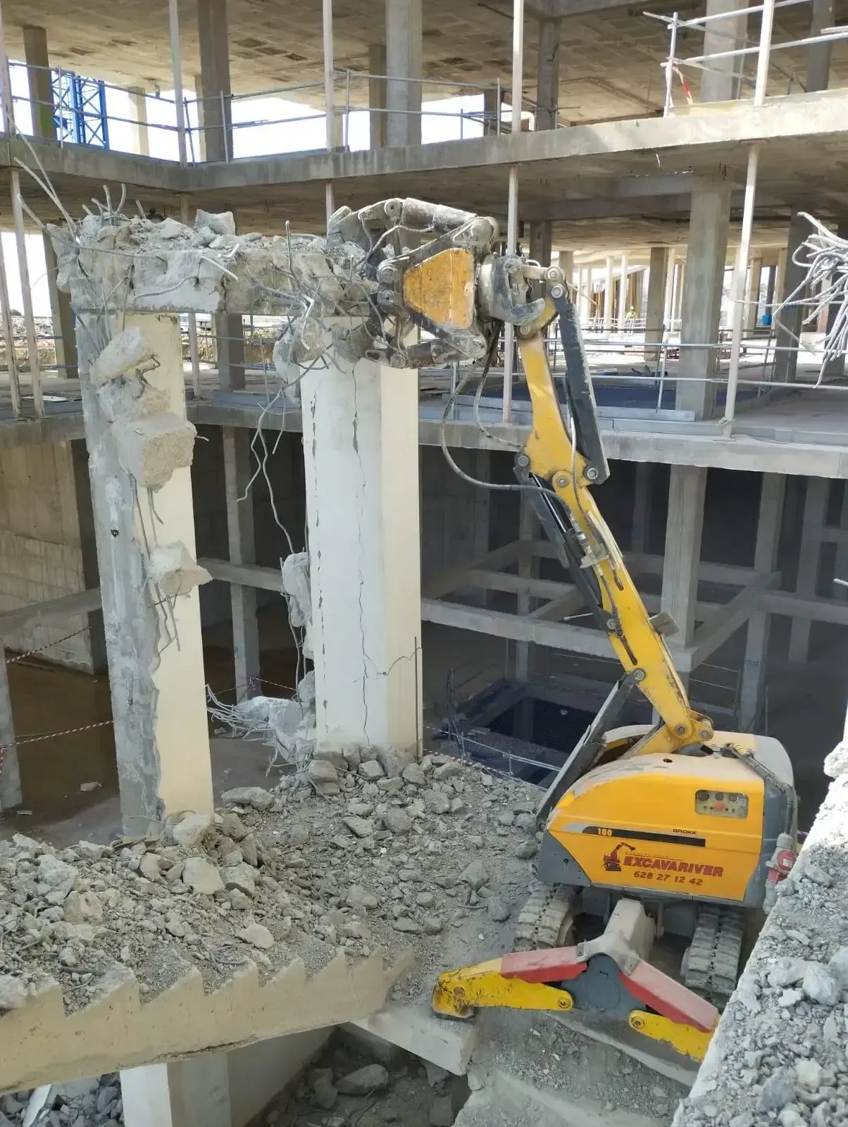 Una excavadora amarilla está rompiendo una columna de hormigón en un edificio en construcción.