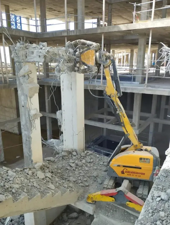 Una excavadora amarilla está rompiendo una columna de hormigón en un edificio en construcción.