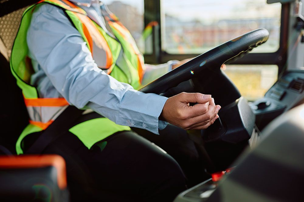 Person in Warnweste fährt einen Bus und hält das Lenkrad.