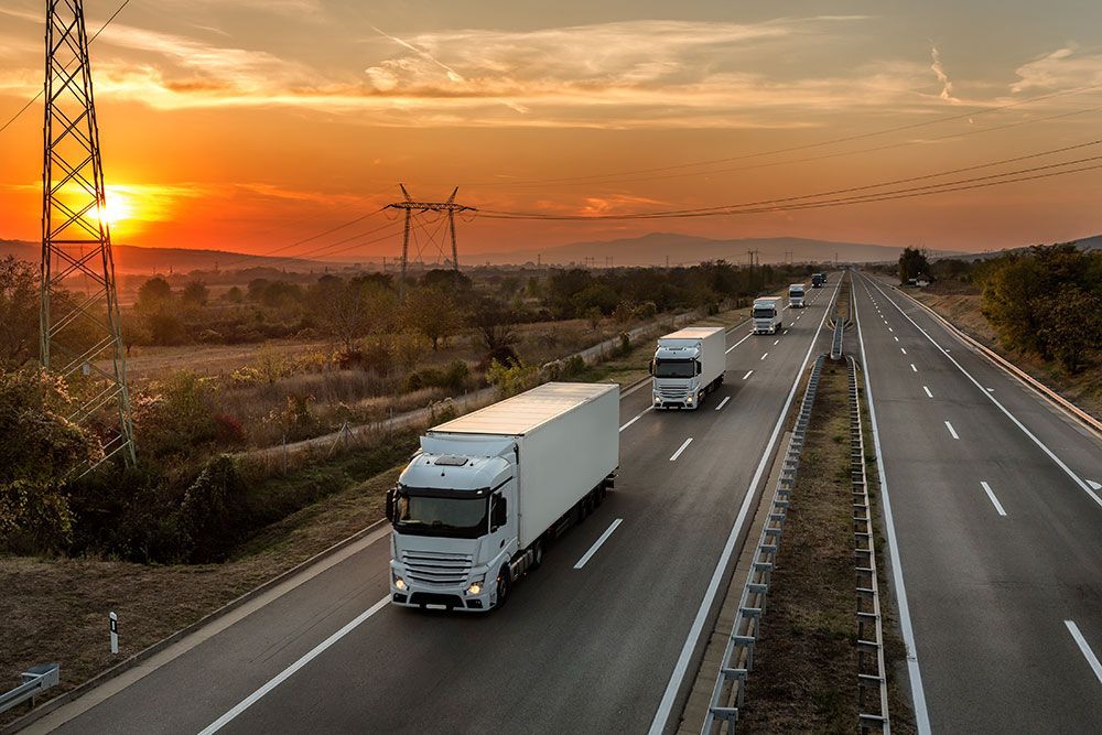 Lastwagen fahren bei Sonnenuntergang auf einer Autobahn mit Stromleitungen im Hintergrund.
