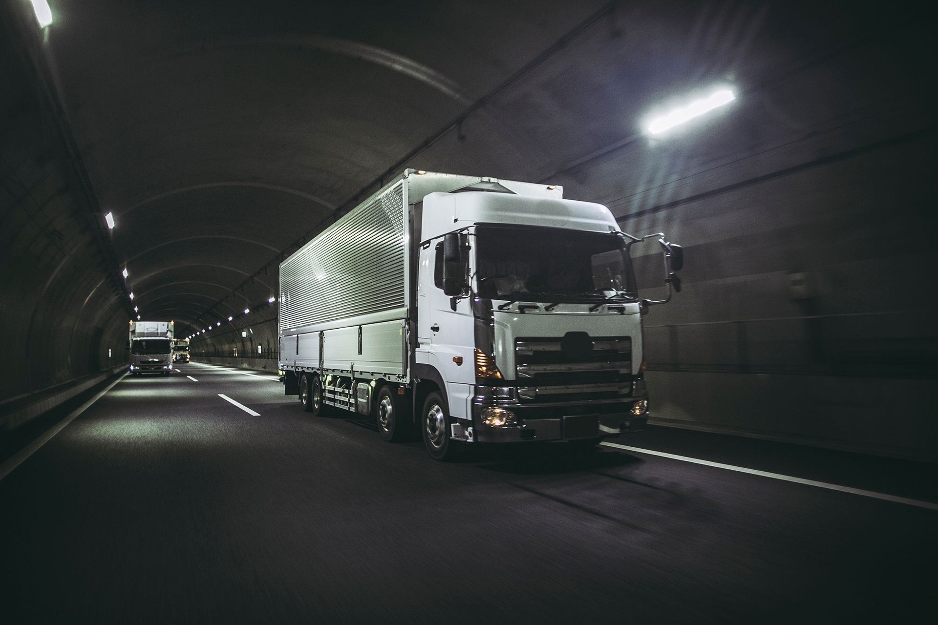 Weißer Sattelschlepper fährt durch einen dunklen Tunnel, beleuchtet von Deckenleuchten.