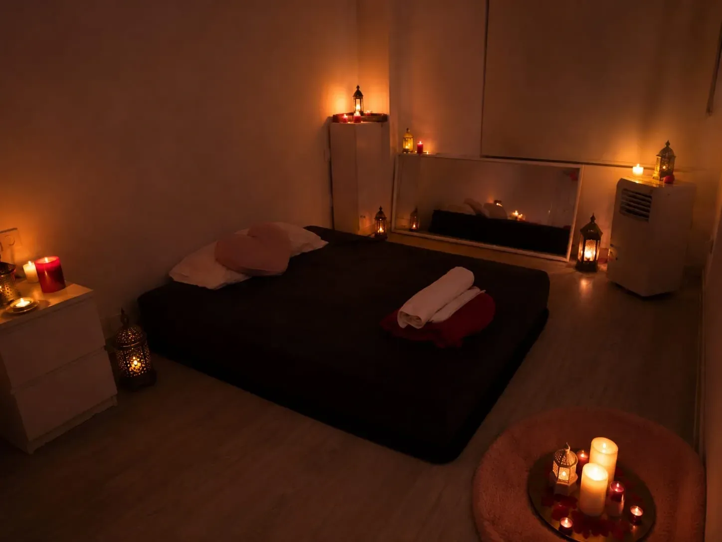 Acogedora habitación iluminada con velas, con una cama baja, luces ámbar cálidas y mesas pequeñas.
