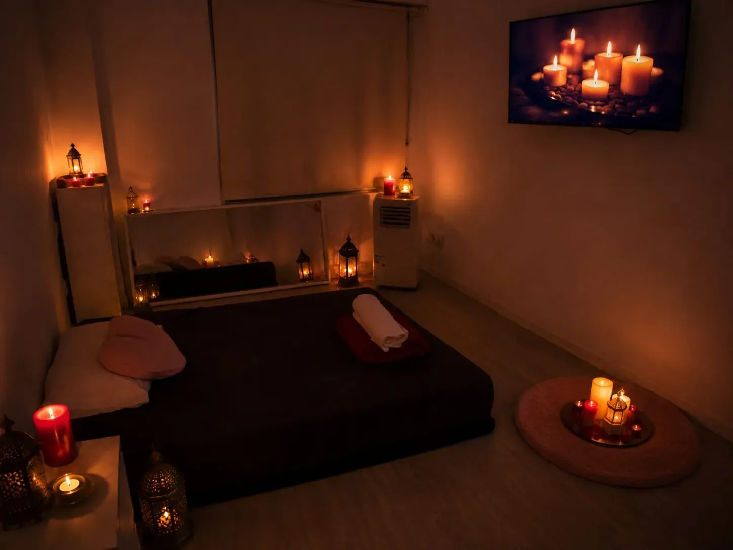 Habitación con luz tenue de velas, cama baja, almohadas y velas en estantes