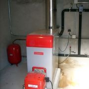 Unidad de calefacción de color rojo y blanco, instalada en un cuarto de servicio con paredes de hormigón.