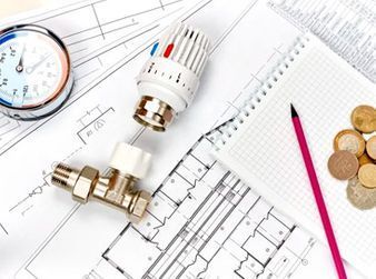 Piezas y herramientas de plomería en planos arquitectónicos con cuaderno, lápiz y monedas.