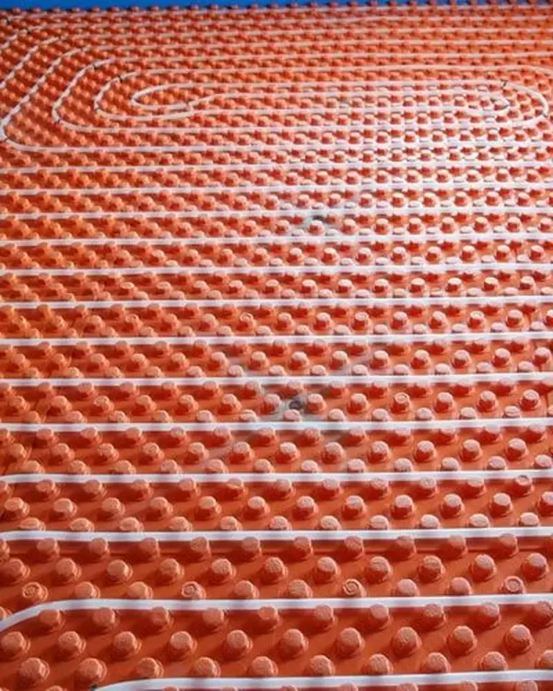 Subsuelo de color naranja con tubos blancos dispuestos en forma de bucle para calefacción por suelo radiante.