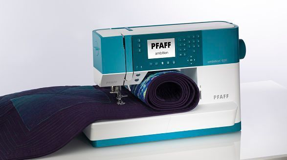 Una máquina de coser Pfaff está sobre una mesa al lado de un rollo de tela.