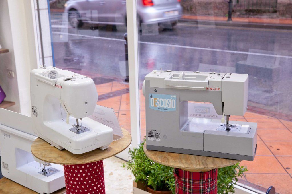 Dos máquinas de coser están sobre una mesa frente a una ventana.