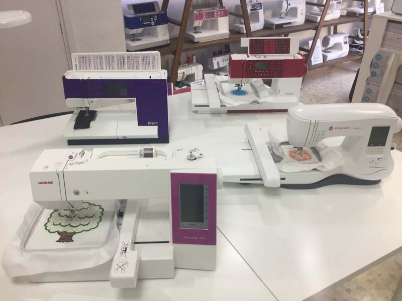 Tres máquinas de coser están sobre una mesa blanca.