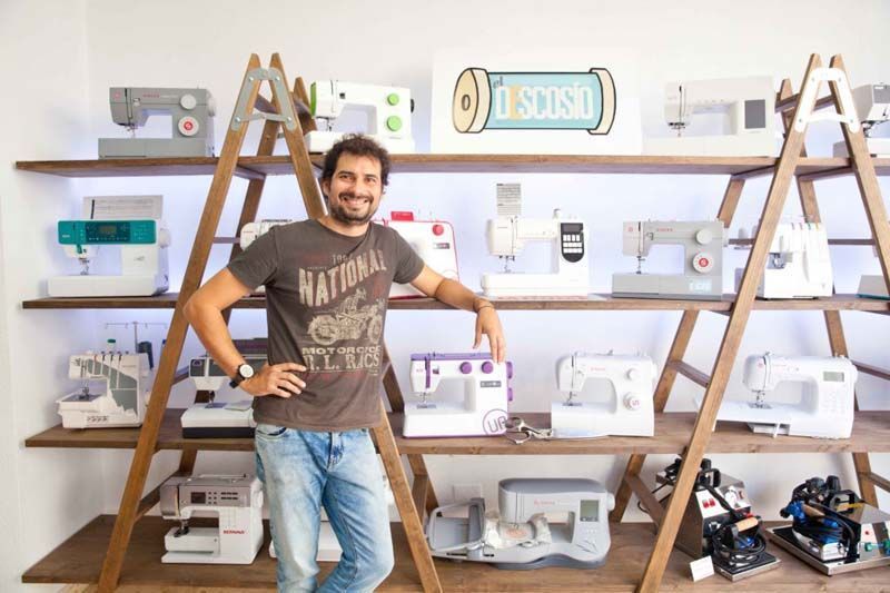 Un hombre está parado frente a un estante lleno de máquinas de coser.