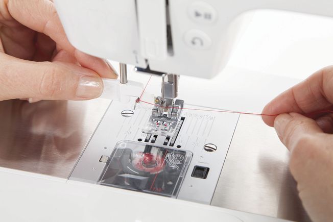 Una máquina de coser Singer blanca está colocada sobre una superficie blanca.