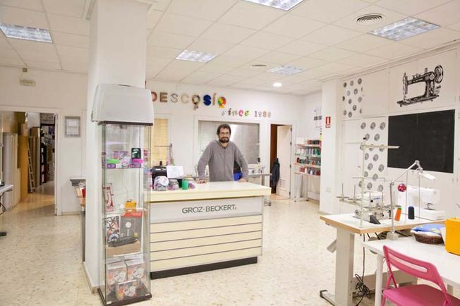 Un hombre está de pie frente a un mostrador en una tienda de costura.