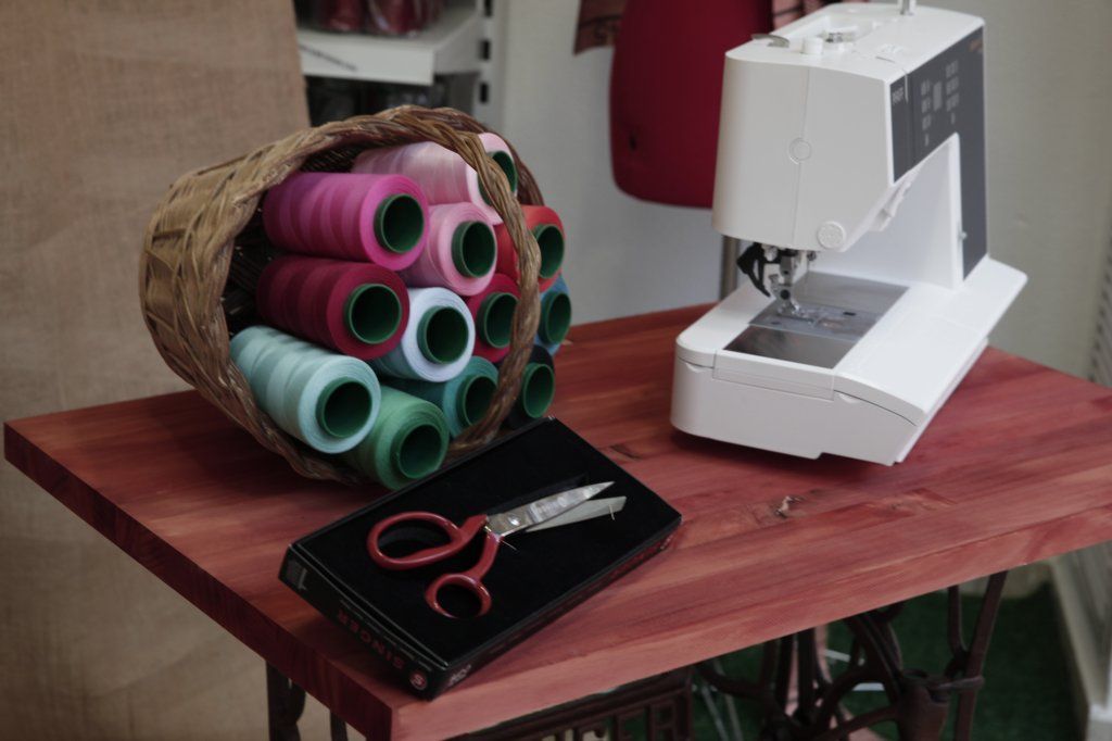 Una máquina de coser se encuentra sobre una mesa junto a una cesta de hilo y tijeras.