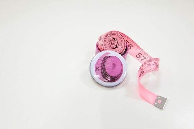 Una cinta métrica rosa y un botón sobre una superficie blanca.