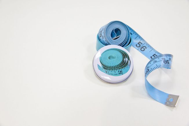 Una cinta métrica rosa y un botón sobre una superficie blanca.