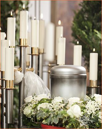 Urna de plata, velas y flores blancas dispuestas para un servicio conmemorativo.