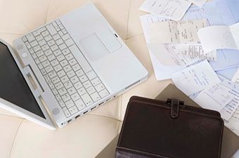 Una computadora portátil, recibos y una agenda sobre una superficie blanca, lo que sugiere una tarea presupuestaria o financiera.