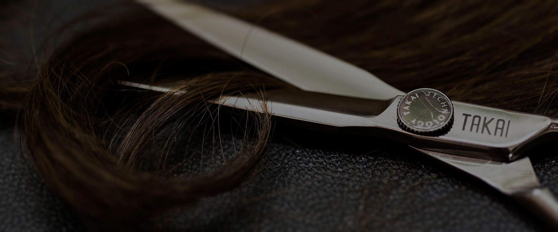 Eine professionelle Haarschneideschere liegt auf einer dunklen Oberfläche neben einer braunen Haarsträhne.
