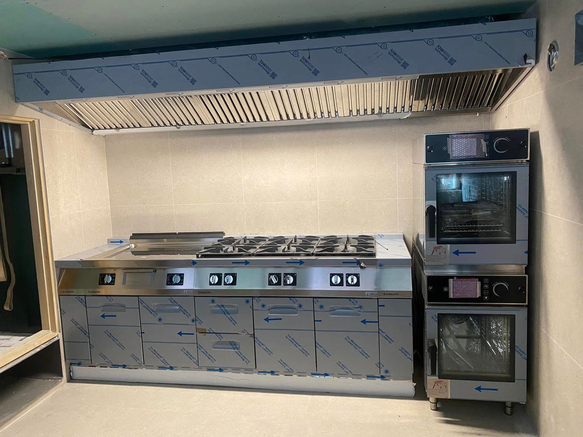 Cuisine professionnelle avec plaque de cuisson en acier inoxydable, hotte aspirante et fours encastrés.