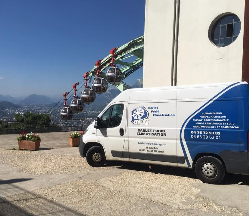 Une camionnette de service blanche est garée à côté d'un bâtiment, avec un téléphérique en arrière-plan.