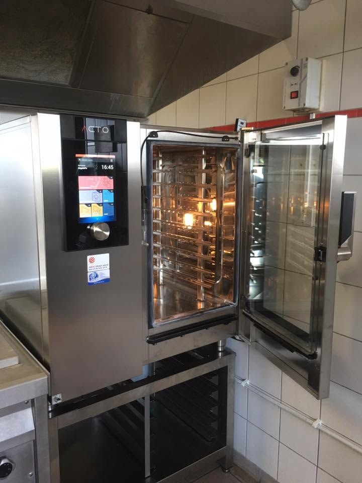 Four professionnel avec porte vitrée ouverte et grilles éclairées dans une cuisine carrelée.