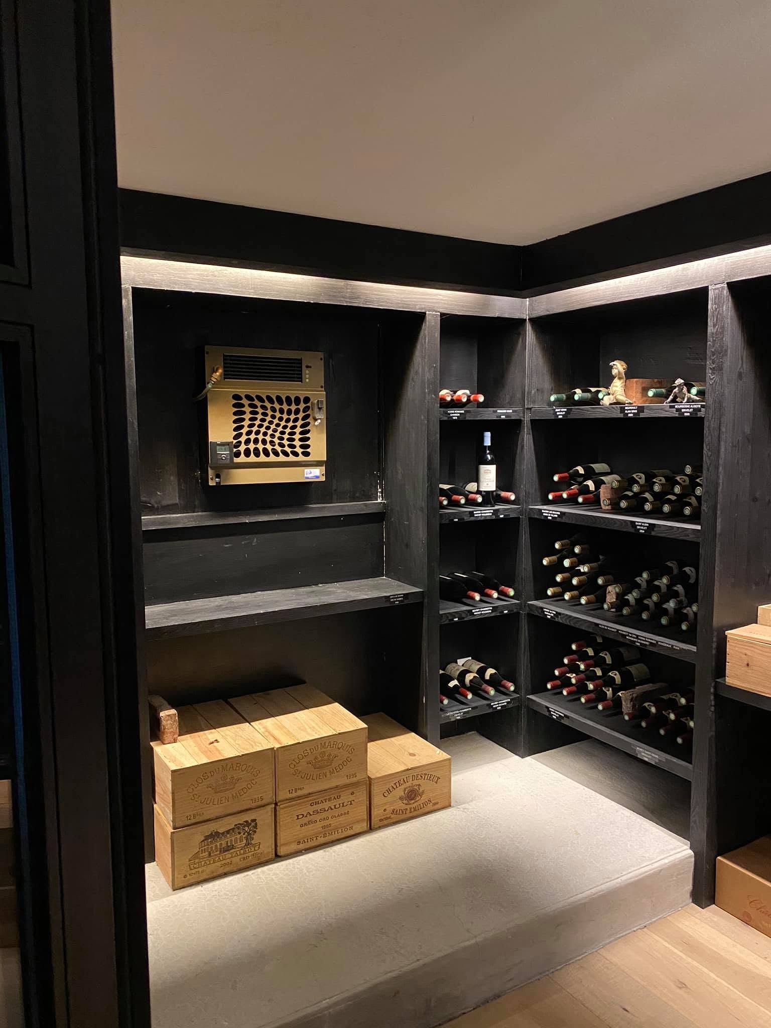 Dressing sombre avec étagères noires, range-bouteilles et boîtes pliées sur un sol gris.
