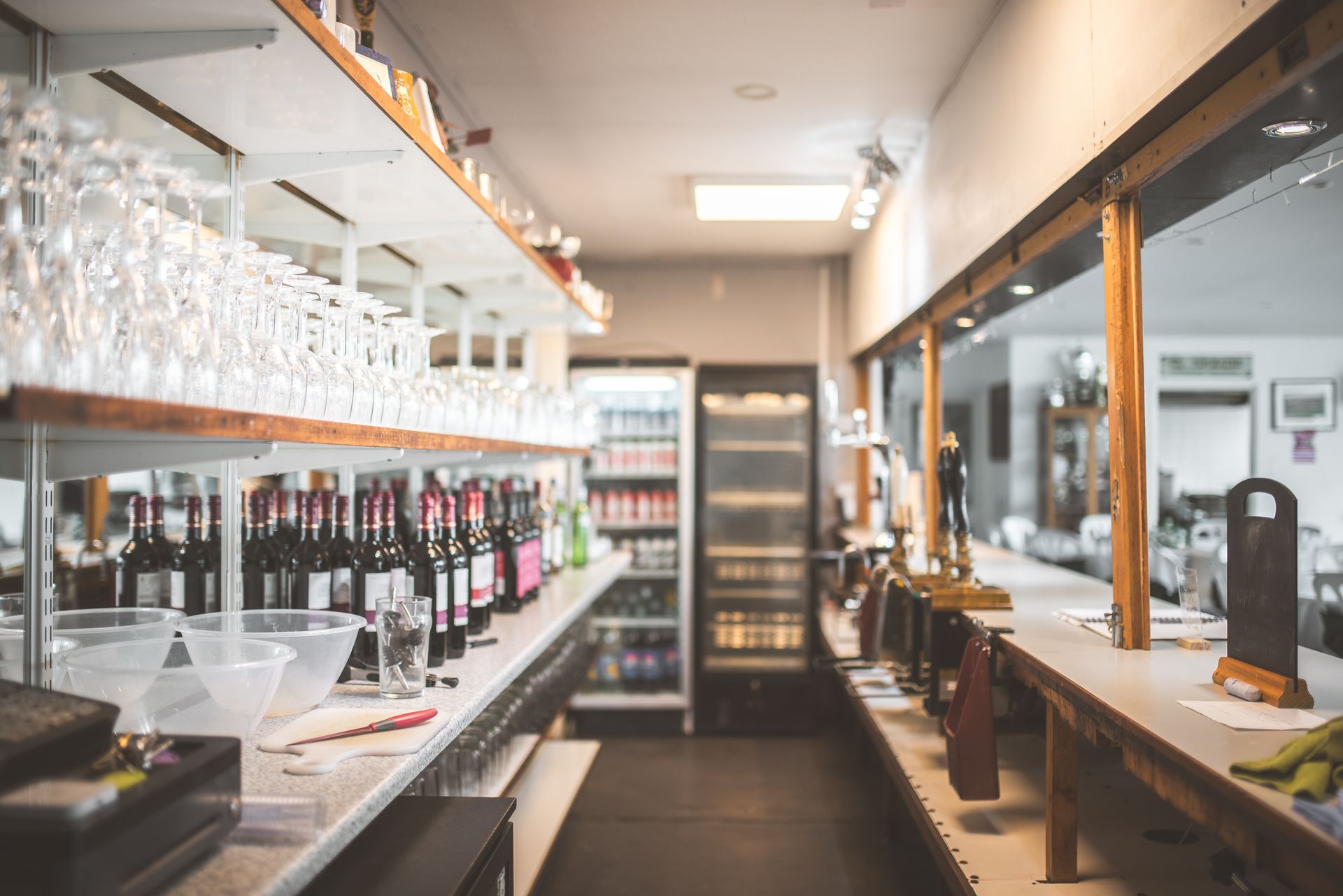 Bar à vin moderne et vide, avec des étagères de bouteilles et de verres le long d'un comptoir lumineux.